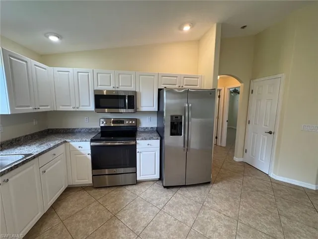 Kitchen featuring stainless steel appliances, white cabinetry, arched walkways, vaulted ceiling, and light tile patterned floors