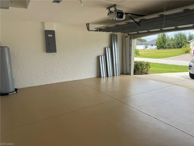 Garage with a textured wall, electric panel, water heater, and a garage door opener