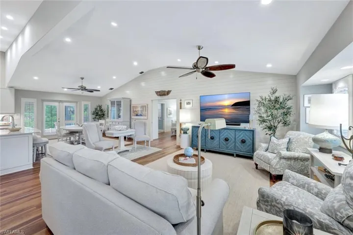 Living room with ceiling fan, vaulted ceiling, wood finished floors, recessed lighting, and wooden walls