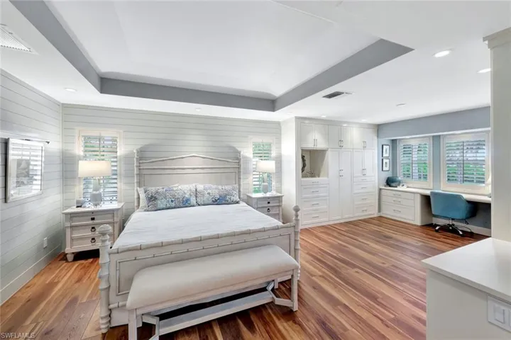 Bedroom with light wood-style flooring, wooden walls, built in study area, a raised ceiling, and recessed lighting