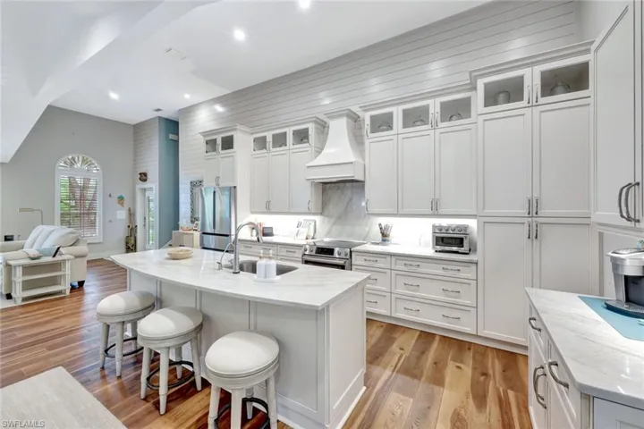 Kitchen with custom exhaust hood, stainless steel appliances, a kitchen bar, open floor plan, and recessed lighting