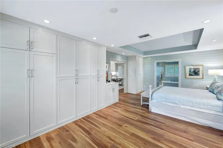 Bedroom with light wood-type flooring, a raised ceiling, and recessed lighting