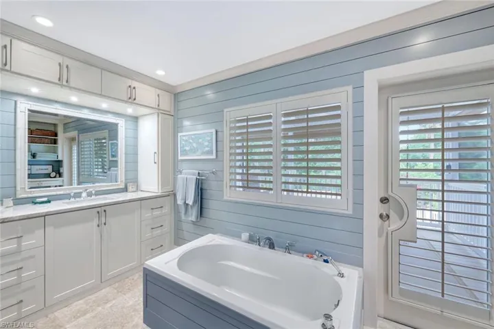Full bath featuring vanity, a garden tub, wood walls, and recessed lighting
