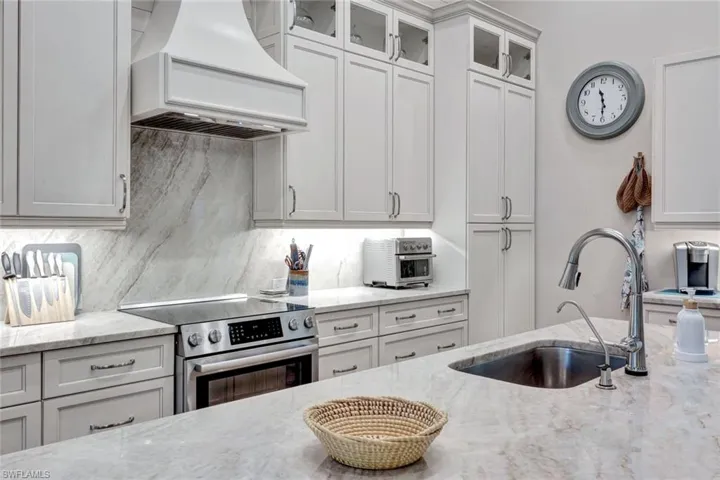 Kitchen featuring stainless steel electric range oven, premium range hood, glass insert cabinets, white cabinets, and light stone countertops