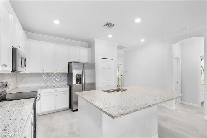 Kitchen featuring sink, white cabinetry, light stone counters, a center island with sink, and stainless steel appliances