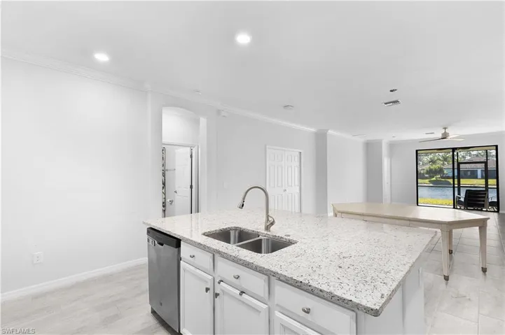 Kitchen with sink, light stone counters, a center island with sink, stainless steel dishwasher, and white cabinets
