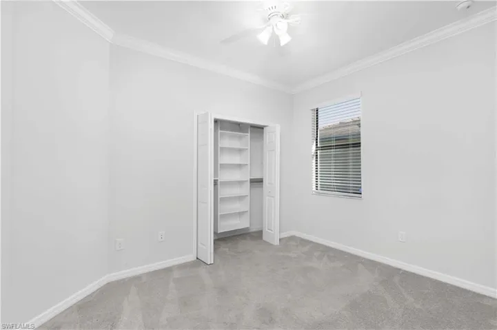 Unfurnished bedroom featuring ceiling fan, ornamental molding, and light colored carpet