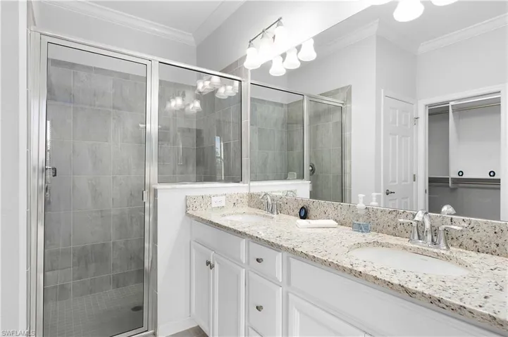 Bathroom featuring a shower with door, vanity, and crown molding