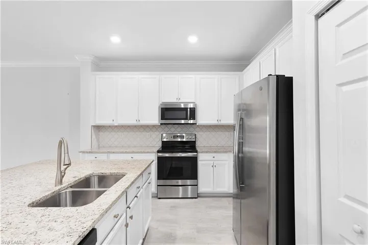 Kitchen featuring light stone countertops, appliances with stainless steel finishes, sink, and white cabinets