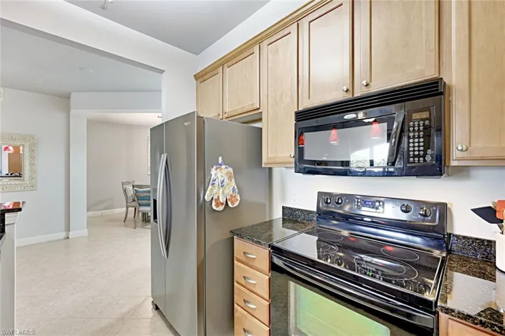 Kitchen with black appliances, dark stone countertops, light tile patterned flooring, and light brown cabinets