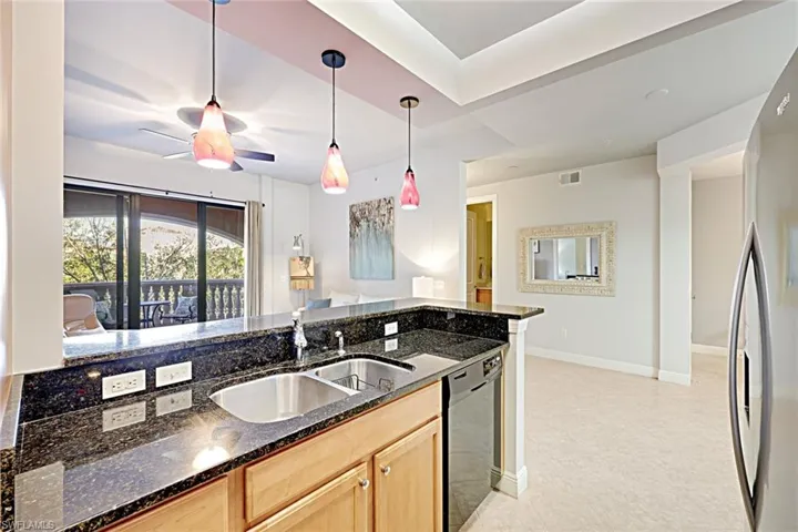 Kitchen featuring dark stone countertops, pendant lighting, black dishwasher, freestanding refrigerator, and light brown cabinetry
