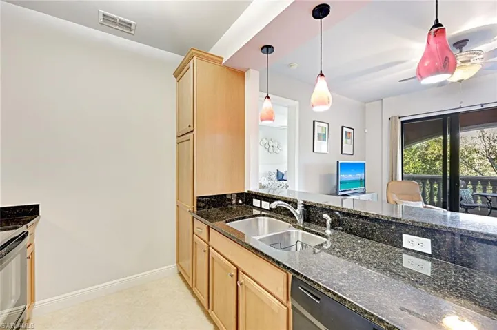Kitchen featuring dark stone counters, pendant lighting, range, dishwashing machine, and light brown cabinets