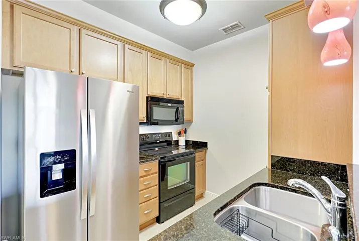 Kitchen with black appliances, dark stone counters, light brown cabinetry, and pendant lighting