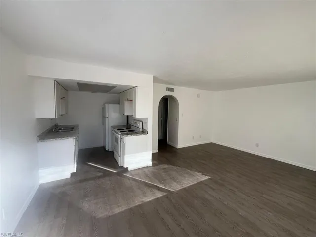 Kitchen with white electric range oven, arched walkways, white cabinets, dark wood finished floors, and open floor plan