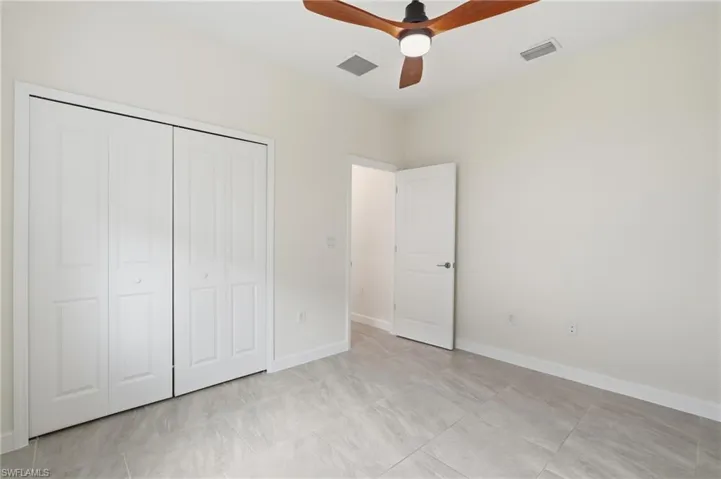 Room featuring light gray tile flooring, crisp white walls, and a wood-finish ceiling fan with integrated lighting