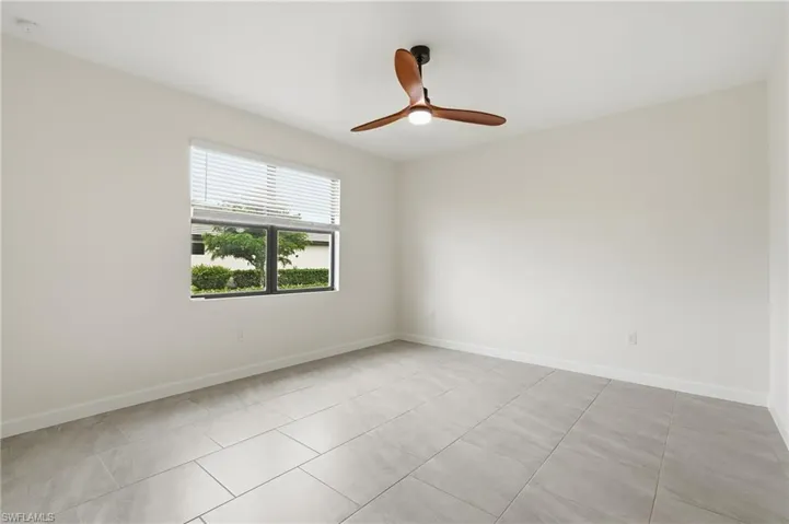 Spacious room featuring light-toned walls, tile flooring, and a modern ceiling fan with wood-finish blades