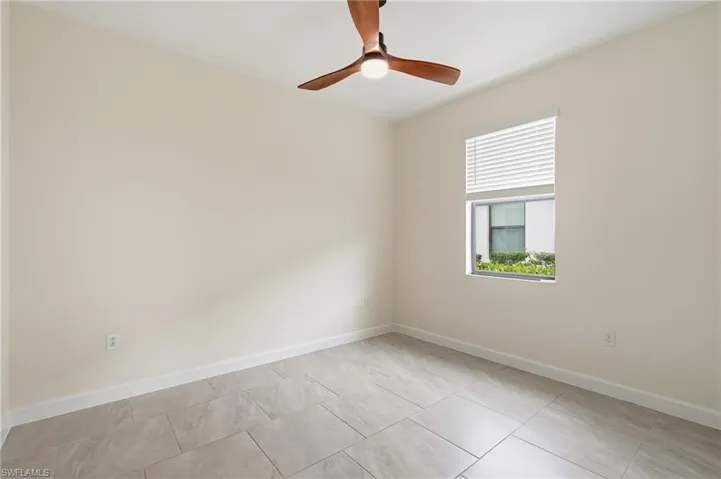 Neutral-toned room featuring a wood-finish ceiling fan with integrated lighting, a window with horizontal blinds, and large format tile flooring