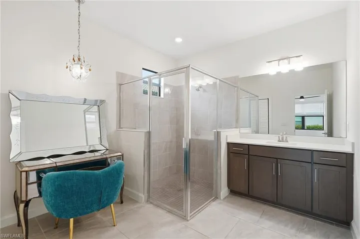 Spacious bathroom featuring a glass-enclosed shower with tile surround, a large vanity with ample storage, a wide mirror, and a contemporary chandelier