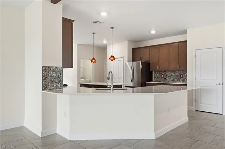 Open-concept kitchen featuring an eat-at counter, stainless steel appliances, dark wood cabinetry, and a decorative tile backsplash
