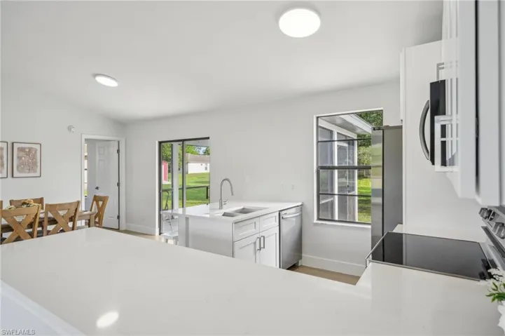 Kitchen with a sink, stainless steel appliances, baseboards, a peninsula, and lofted ceiling