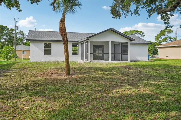 Back of property featuring a sunroom, stucco siding, a yard, and a shingled roof