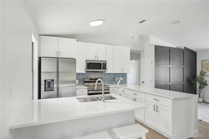 Kitchen featuring appliances with stainless steel finishes, a peninsula, a sink, lofted ceiling, and light countertops
