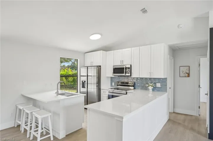 Kitchen featuring stainless steel appliances, a peninsula, a sink, light wood-type flooring, and vaulted ceiling