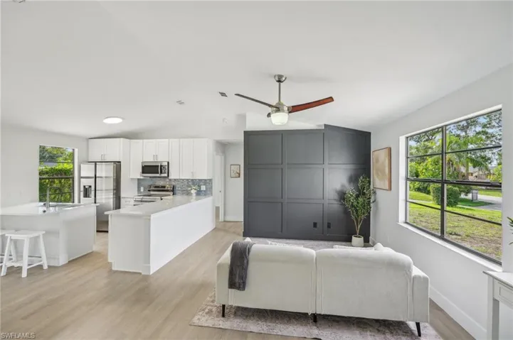 Living room featuring vaulted ceiling, plenty of natural light, light wood finished floors, a ceiling fan, and baseboards