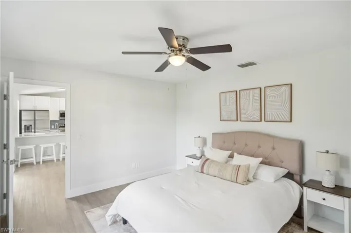 Bedroom with stainless steel fridge, light wood-style floors, ceiling fan, baseboards, and a sink