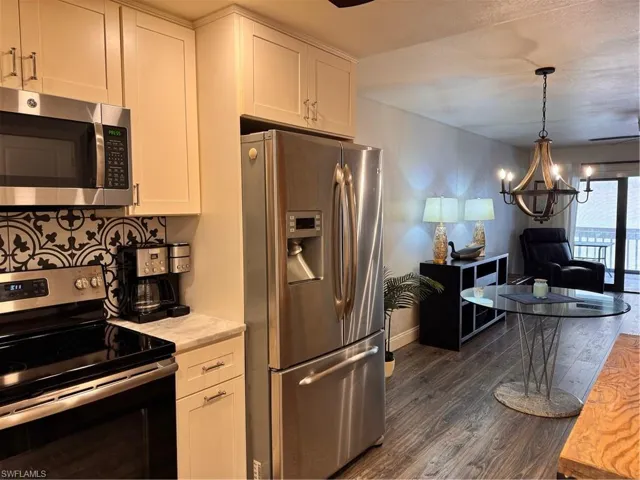 Kitchen with appliances with stainless steel finishes, white cabinets, a chandelier, dark wood finished floors, and decorative backsplash