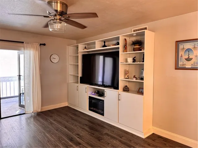 Unfurnished living room featuring dark wood-style floors, ceiling fan, and a textured ceiling