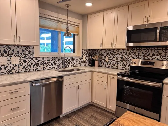 Kitchen with stainless steel appliances, white cabinets, backsplash, light stone counters, and recessed lighting