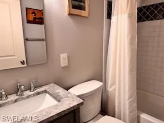 Bathroom with shower / bathtub combination with curtain, vanity, and a textured wall