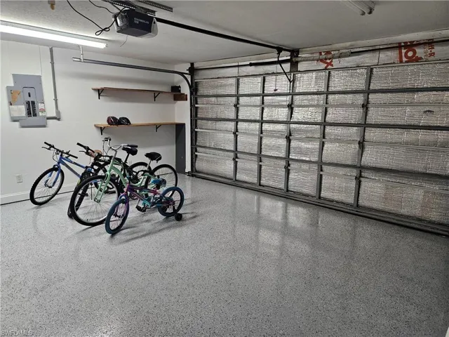 Garage with electric panel, a garage door opener, and baseboards