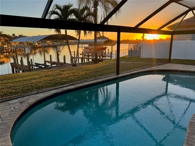 Pool at dawn with a dock, fence, glass enclosure, and a water view