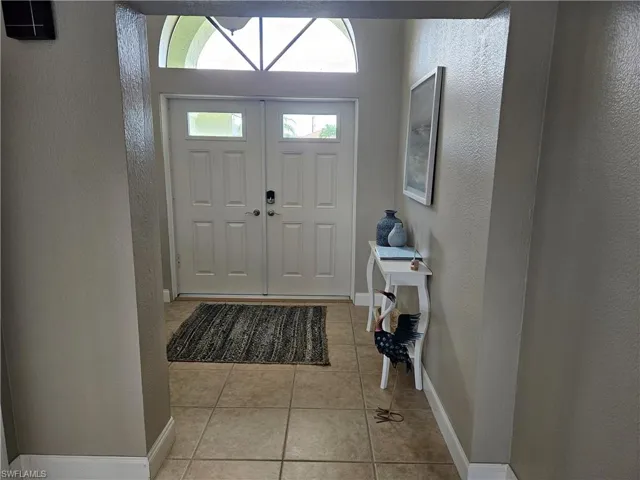 Entrance foyer with light tile patterned floors, a textured wall, and baseboards