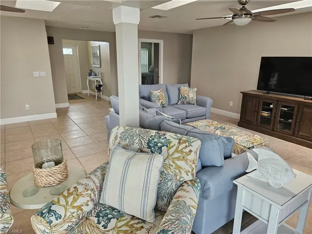 Living room featuring visible vents, a skylight, baseboards, a ceiling fan, and light tile patterned floors