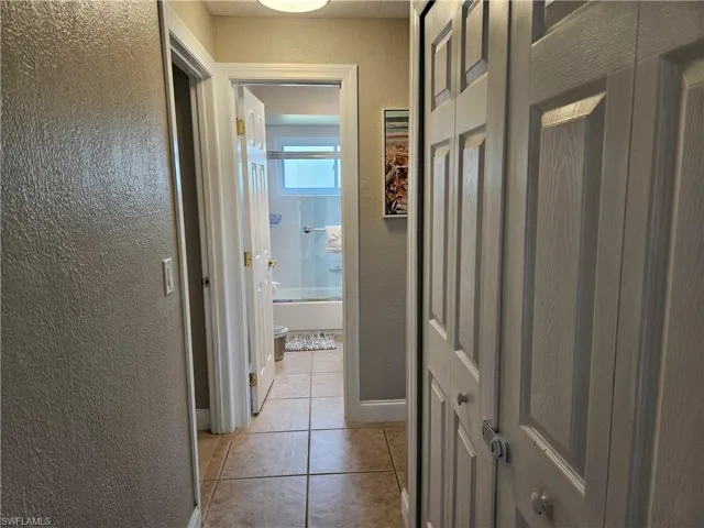 Hall with baseboards, a textured wall, and light tile patterned floors