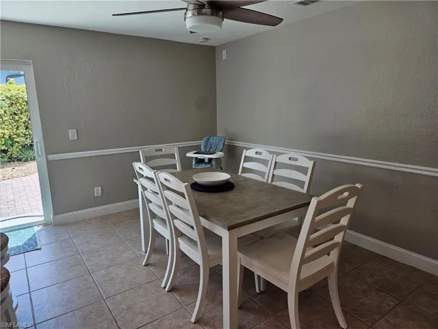 Tiled dining space featuring baseboards, visible vents, a textured wall, and a ceiling fan