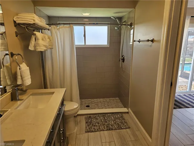 Full bath featuring baseboards, toilet, vanity, tiled shower, and wood tiled floor