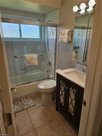 Full bath featuring bath / shower combo with glass door, toilet, tile patterned flooring, and vanity