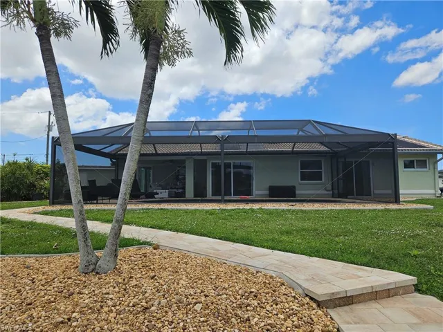 Rear view of house with stucco siding, a lanai, and a lawn