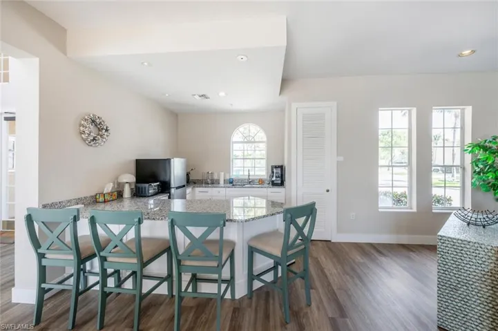 Kitchen with light stone counters, dark wood-style flooring, freestanding refrigerator, a peninsula, and white cabinetry
