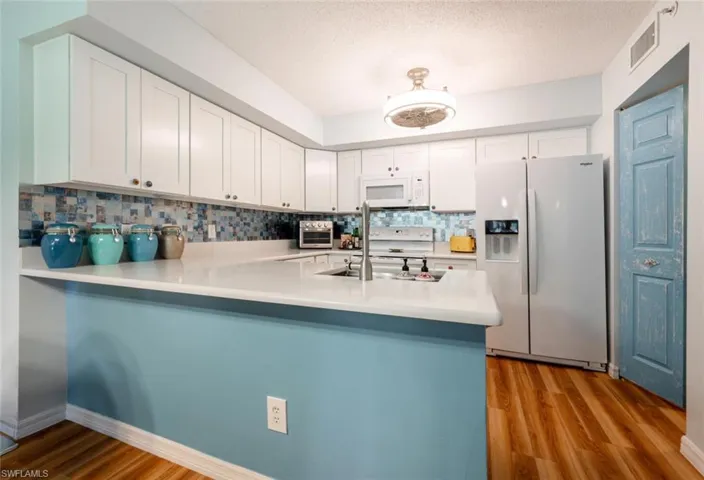 Kitchen with visible vents, backsplash, wood finished floors, white appliances, and a peninsula