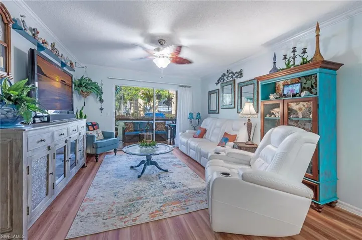 Living room featuring ceiling fan, a textured ceiling, ornamental molding, and wood finished floors