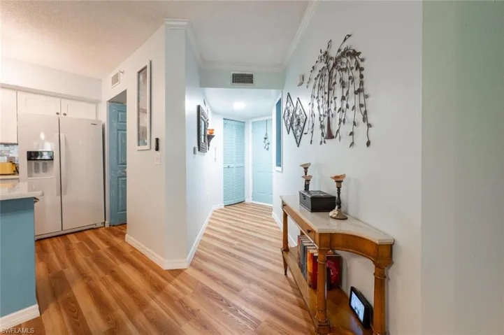 Hall featuring light wood-style flooring, visible vents, baseboards, and ornamental molding