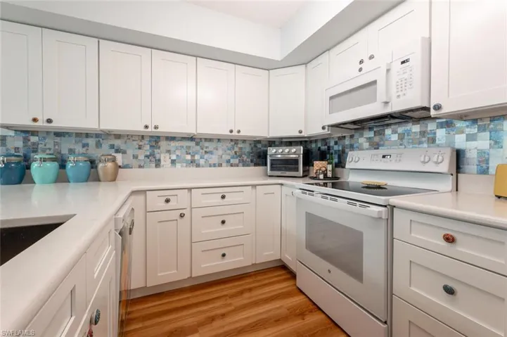 Kitchen featuring white appliances, white cabinets, light wood-style floors, light countertops, and tasteful backsplash