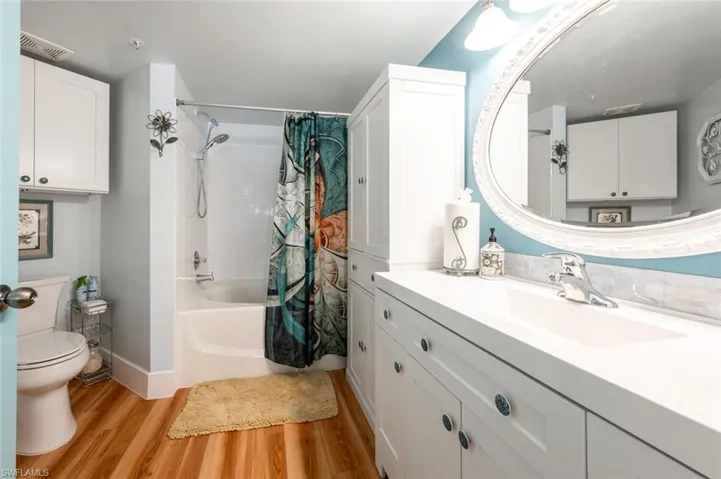 Full bathroom featuring visible vents, toilet, wood finished floors, shower / tub combo with curtain, and vanity