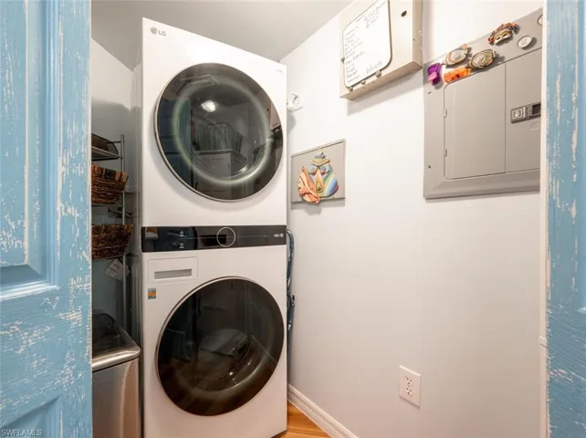 Laundry area featuring laundry area, stacked washing maching and dryer, electric panel, and baseboards