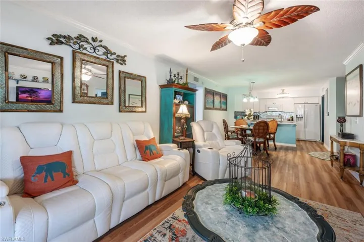 Living room featuring light wood-type flooring, ceiling fan, visible vents, and ornamental molding